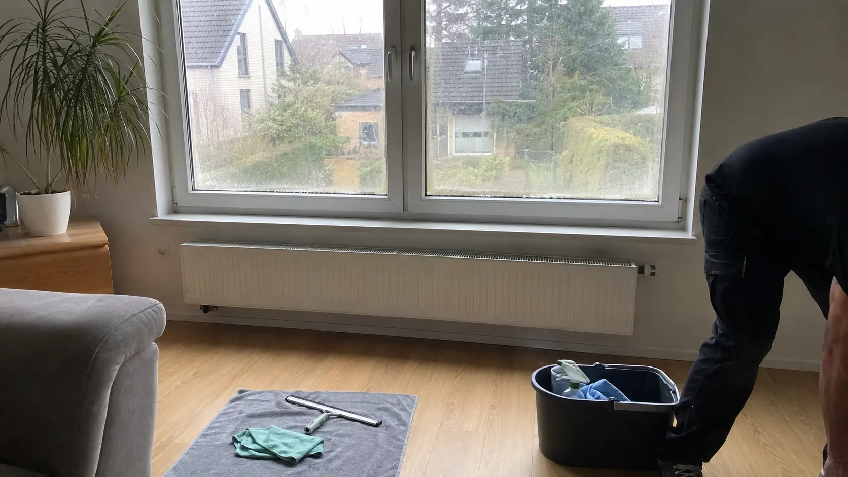 Abzieher, Tuch und Eimer liegen bereit für die Fensterreinigung im Wohnzimmer